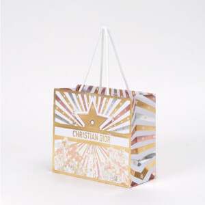 フランスのラグジュアリーブランド。中央に大きなゴールドのスターとロゴを配し、放射状のメタリックストライプとサーカス風イラストが広がる、ホワイトロープハンドル付きのホリデー限定オリジナル紙袋