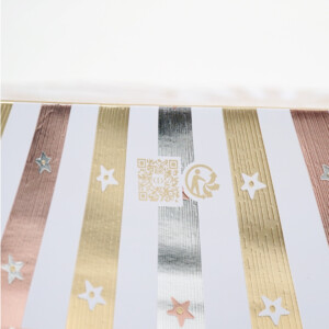 ゴールド・ピンク・シルバーのメタリックストライプに星モチーフとQRコード、リサイクルマークを配した、サステナブルな取り組みを表現するホリデー限定オリジナル紙袋